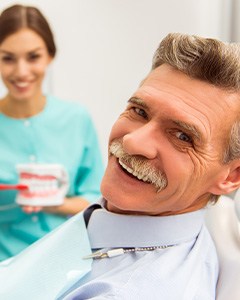 Dentist showing patient in blue collared shirt how to brush dentures