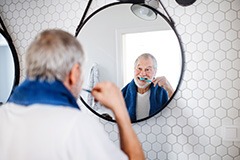 Man brushing teeth in bathroom mirror with blue towel around neck