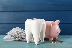  A ceramic model tooth, piggy bank and money on light blue wooden table