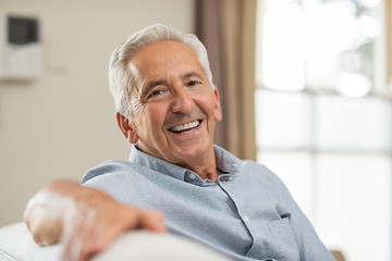 older person with dentures sitting on couch smiling