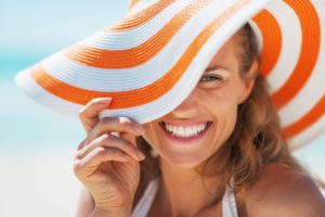 smiling woman pulling the brim of her orange and white striped sun hat